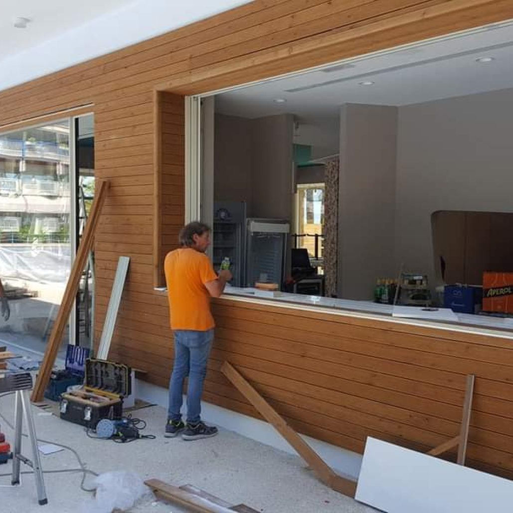 Operai al lavoro sulla facciata del ristorante con rivestimenti in legno.