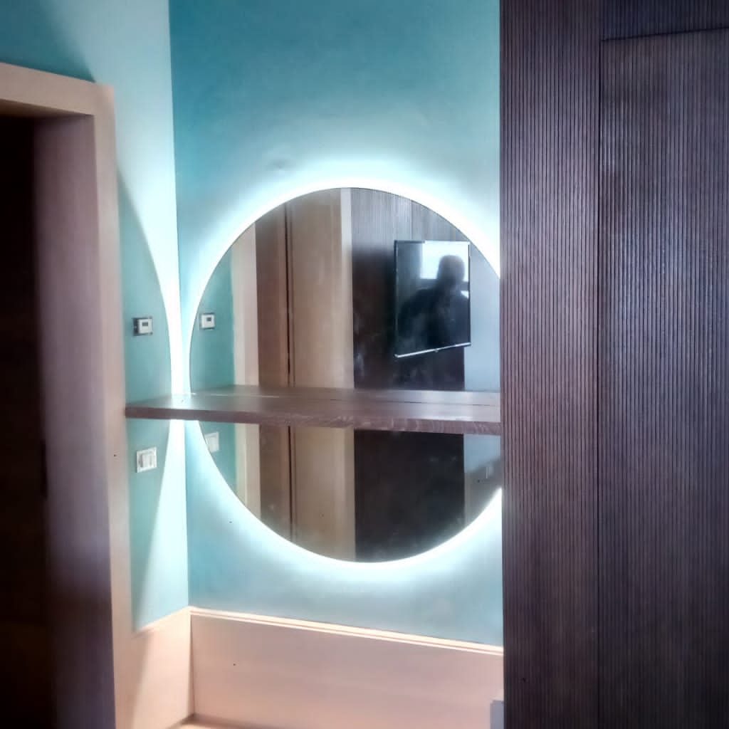 Specchio rotondo retroilluminato con LED su parete blu in una camera d'hotel.